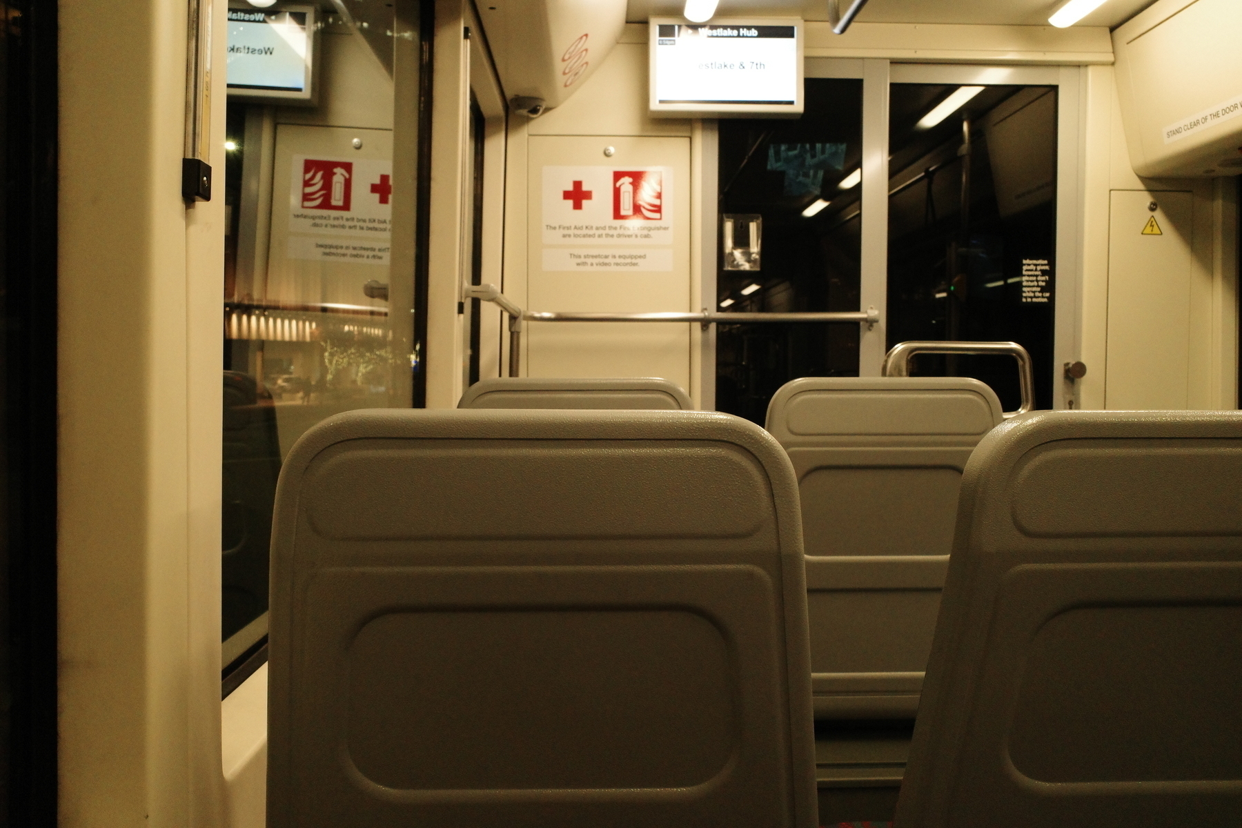 A dimly-lit, empty tram interior with overhead monitors and safety signs is visible.